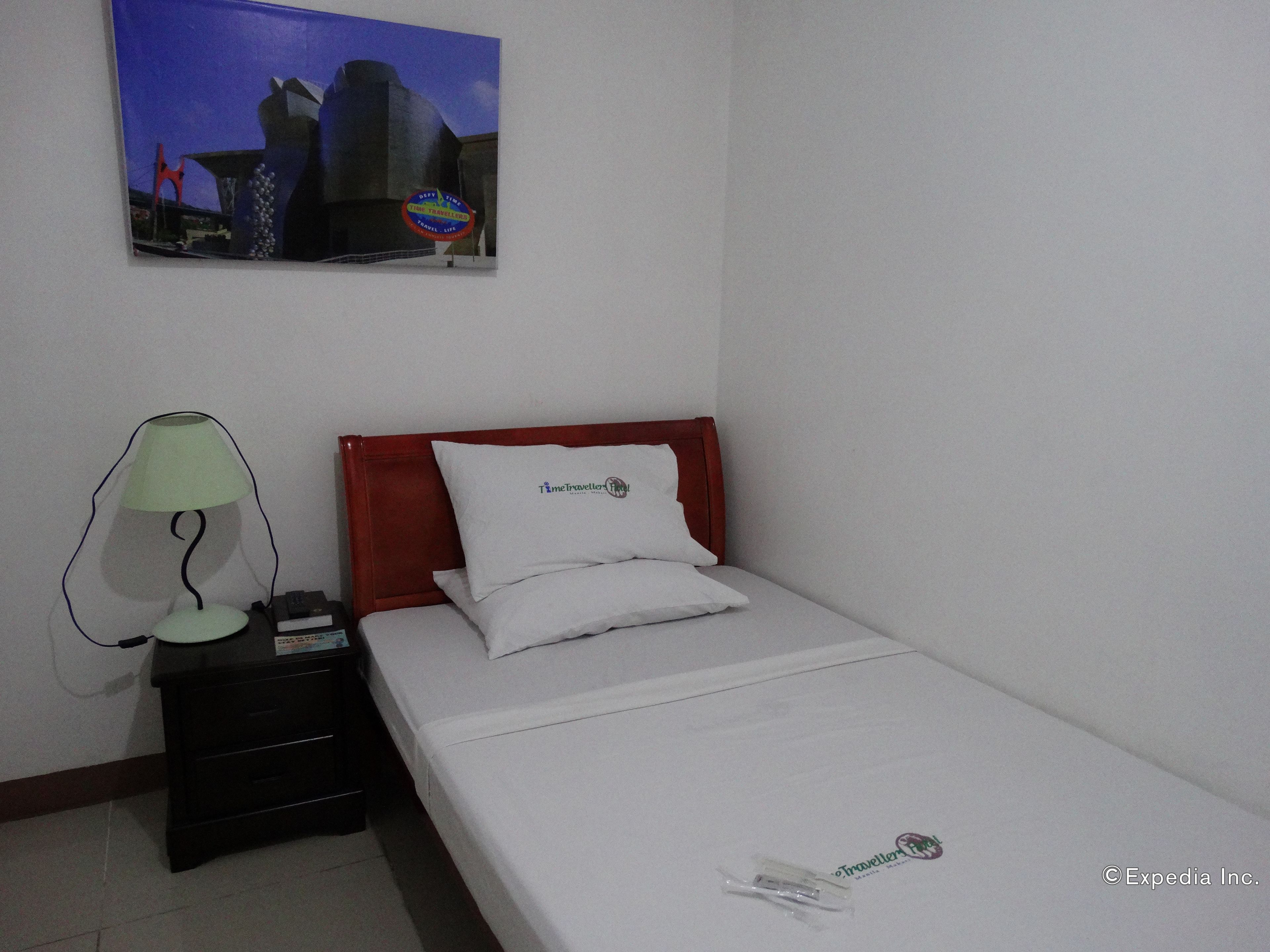 A hotel room with a bed, a nightstand, a lamp, and a painting on the wall.