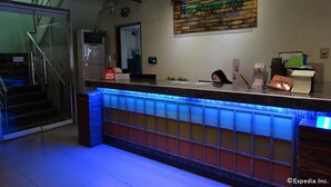 Zona de recepción de un hotel con mostrador, un cartel encima y una escalera con señal de 'tirar'.