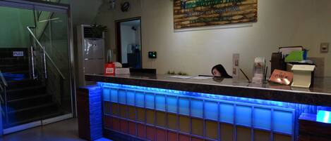 A hotel reception area with a counter, a sign above it, and a staircase with a pull sign.