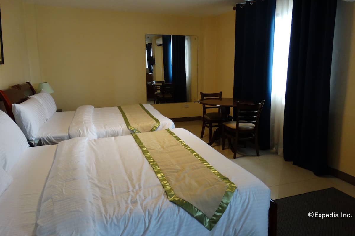 A hotel room with two beds, a desk, a chair, a mirror, and a window with curtains.