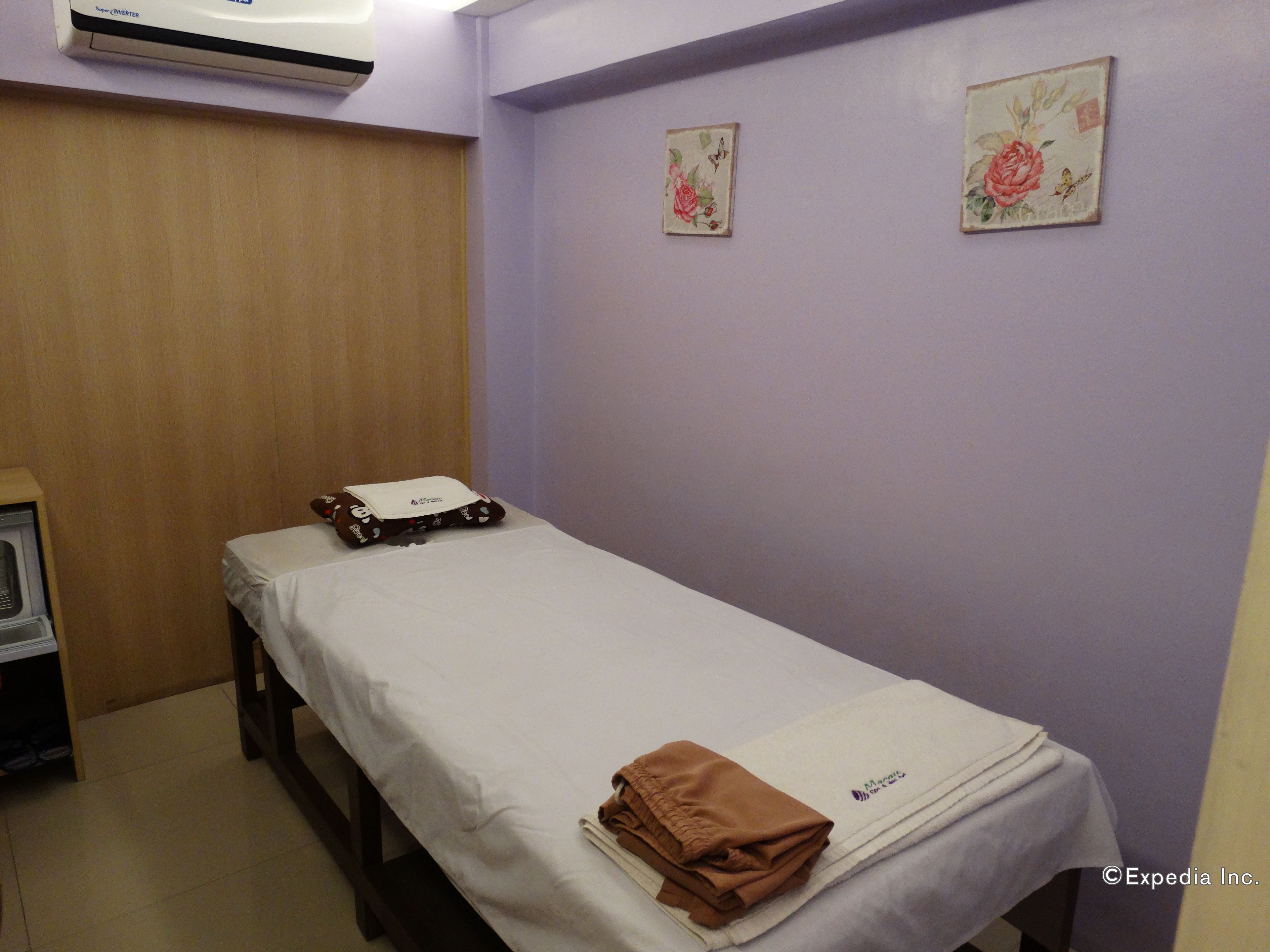 A single bed with a white sheet and a brown towel, a small table with a telephone, and two floral paintings on the wall.