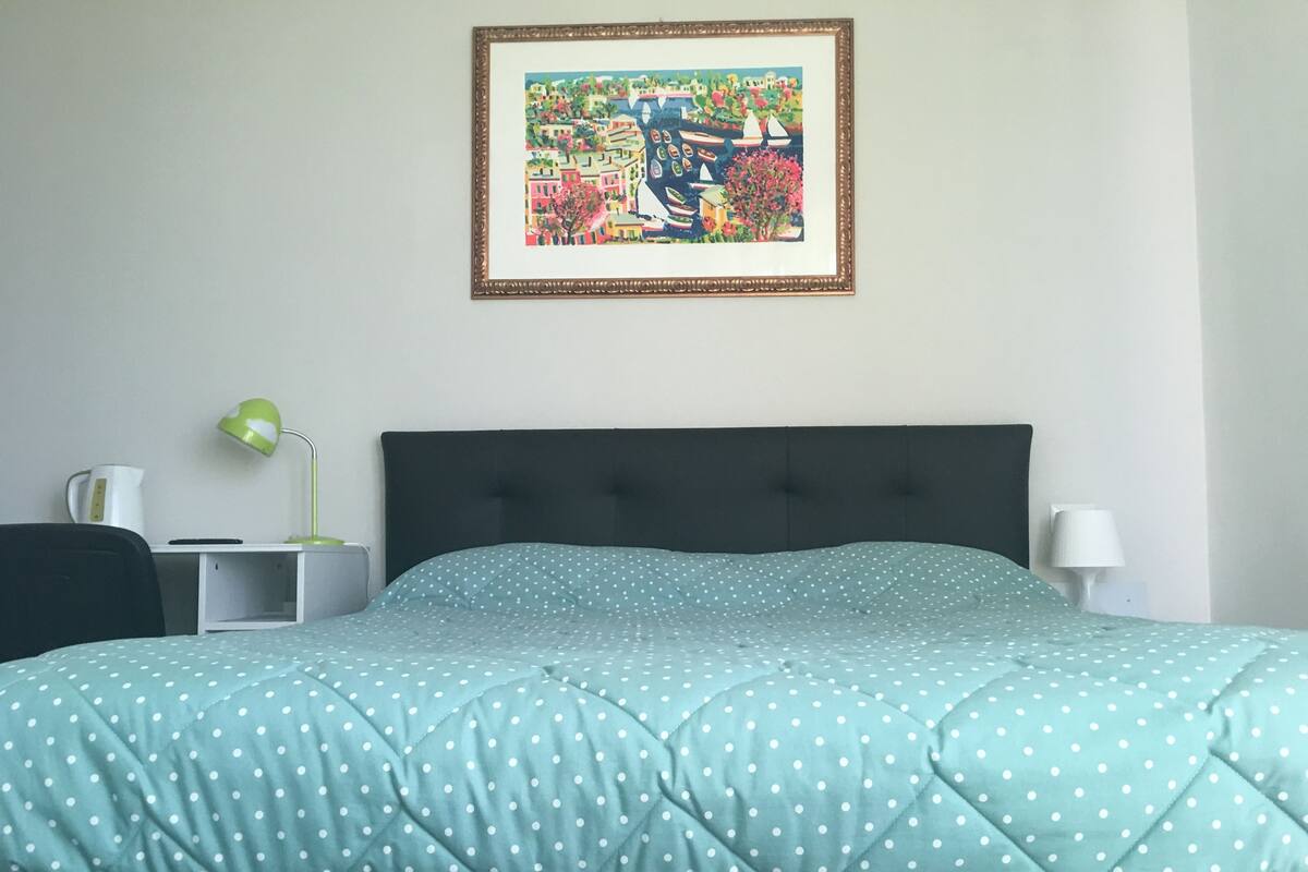A neatly made bed with a polka dot duvet, a framed painting on the wall, and bedside lamps.