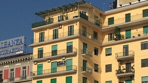 A multi-story building with balconies, a sign for 'LEANZA INIGURAZIONI', and a 'Paradise' sign. - Top Floor (Naples)