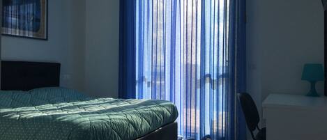 A bedroom with a bed, a chair, a desk, and a window with blue curtains.