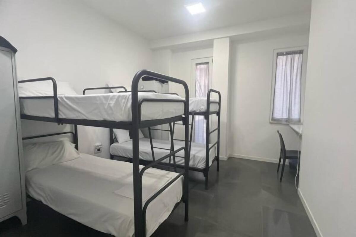A dormitory room with bunk beds, a desk, and a window with curtains.