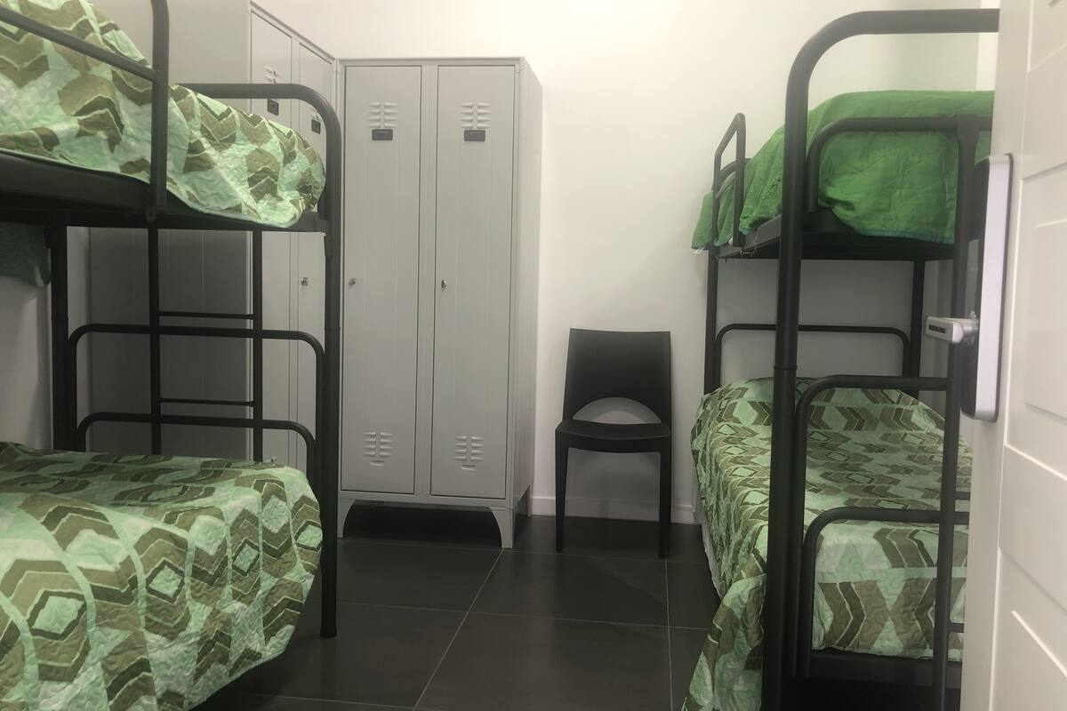 A dormitory room with bunk beds, a wardrobe, and a chair.