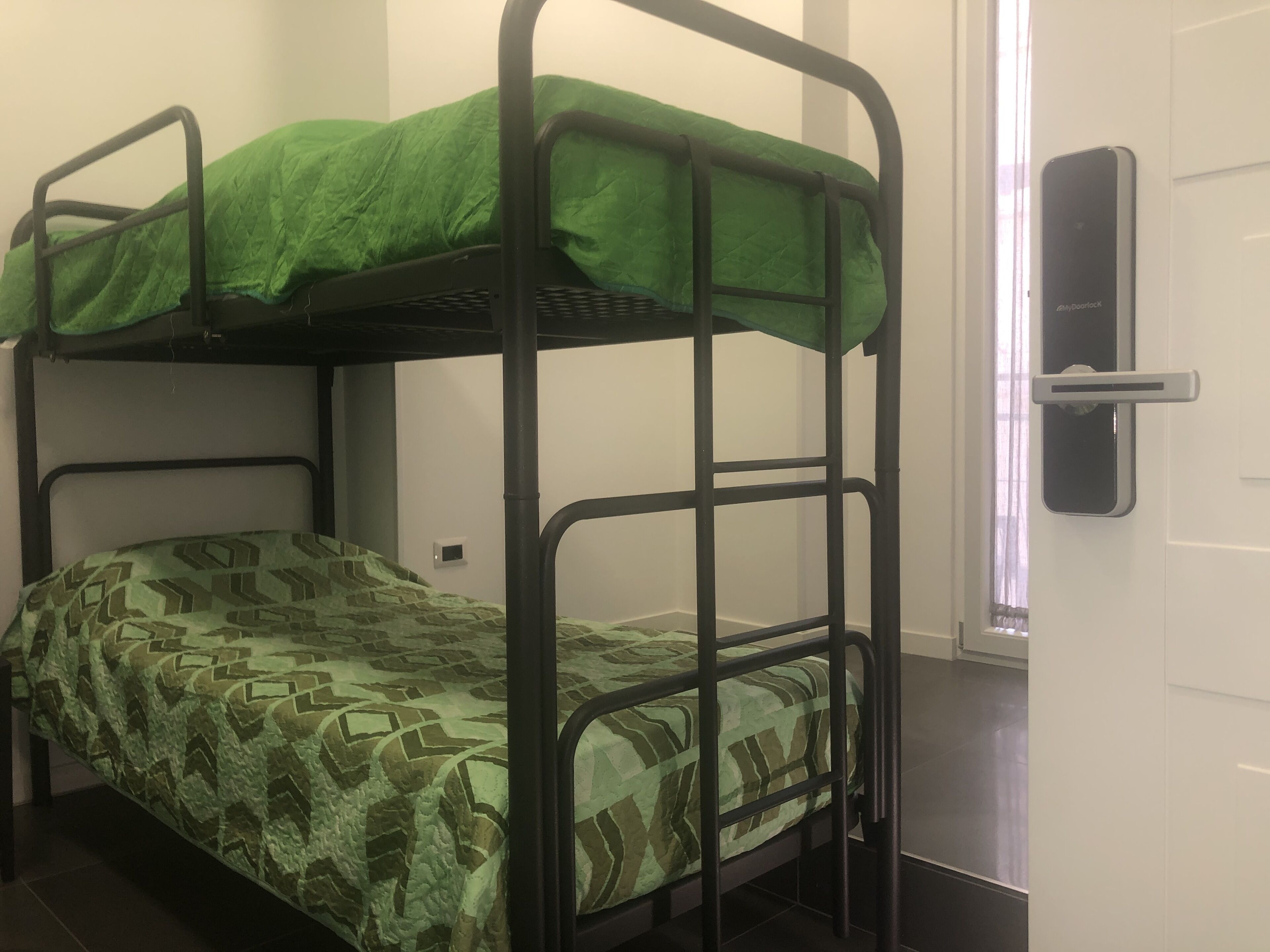 A bunk bed with green bedding, a door with a handle, and a small electrical outlet on the wall.
