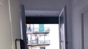 A room with a sliding door, a window with a view of a building with balconies, and a patterned rug on the floor. - Top Floor (Naples)