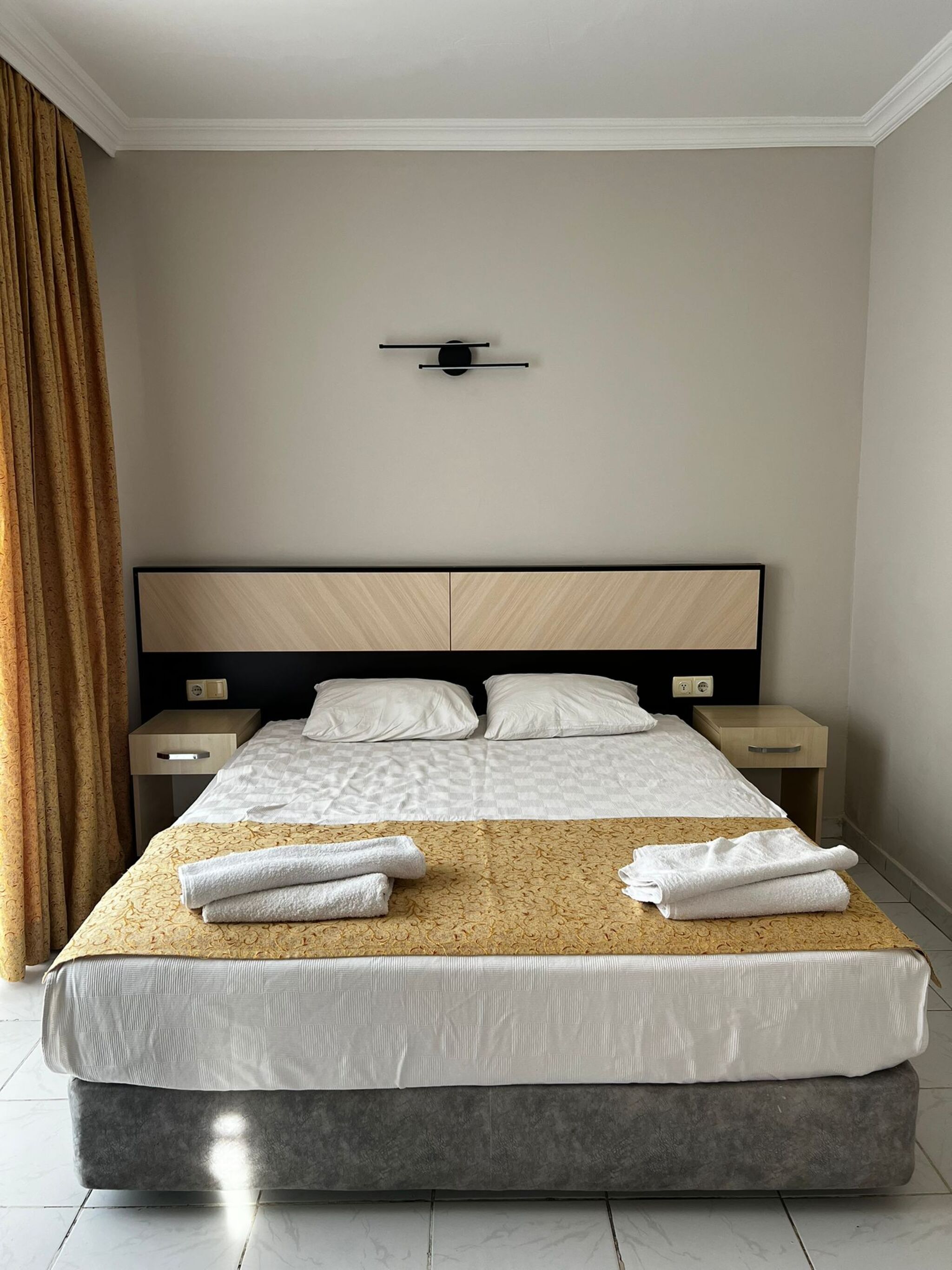 A modern hotel room with a large bed, two bedside tables, and a wall-mounted light fixture.