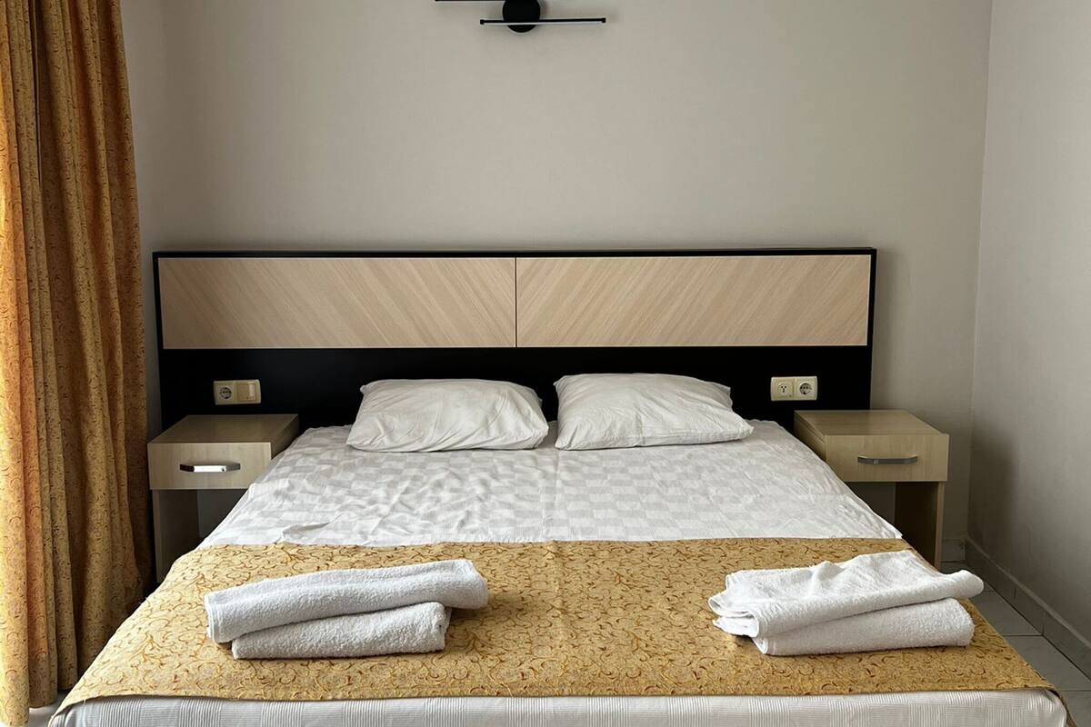Una habitación de hotel moderna con una cama grande, dos mesitas de noche y una lámpara de pared.