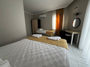 Habitación de hotel con una cama grande, dos camas más pequeñas, un escritorio, un armario, un equipo de aire acondicionado y un espejo.