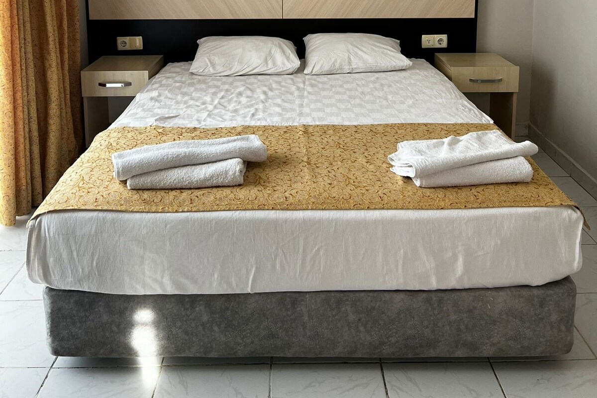 A modern hotel room with a large bed, two bedside tables, and a wall-mounted light fixture.