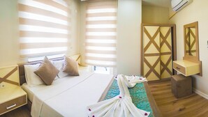 Quarto de hotel com cama, mesas de cabeceira, toucador com espelho e janela com persianas.