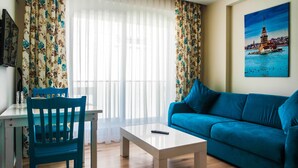 Uma sala de estar com um sofá azul, uma mesa de centro branca, uma cadeira azul e um quadro de uma torre na parede.