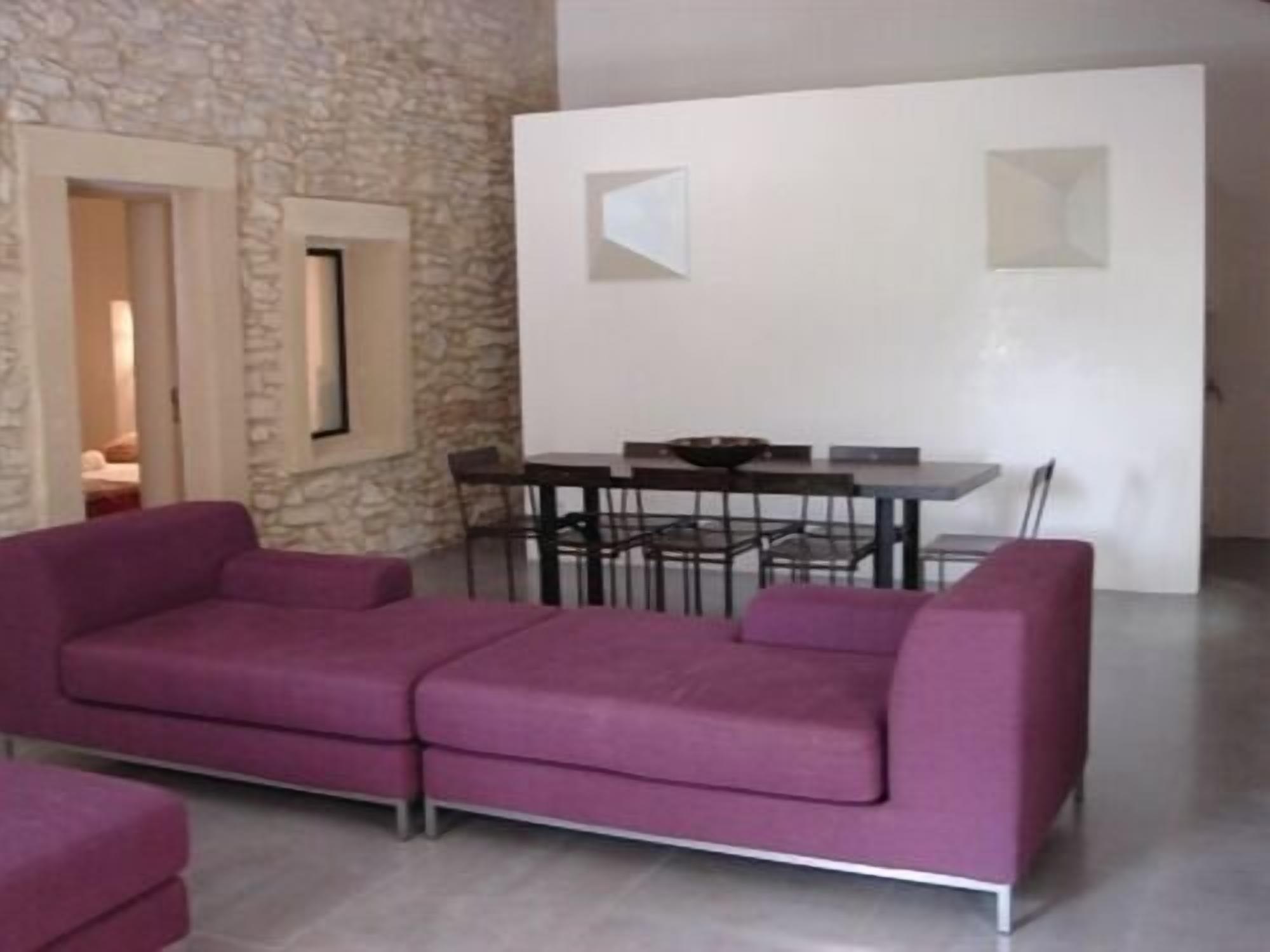 Uma sala de estar moderna com uma parede de pedra, um sofá roxo, uma mesa de jantar com cadeiras e uma porta branca.