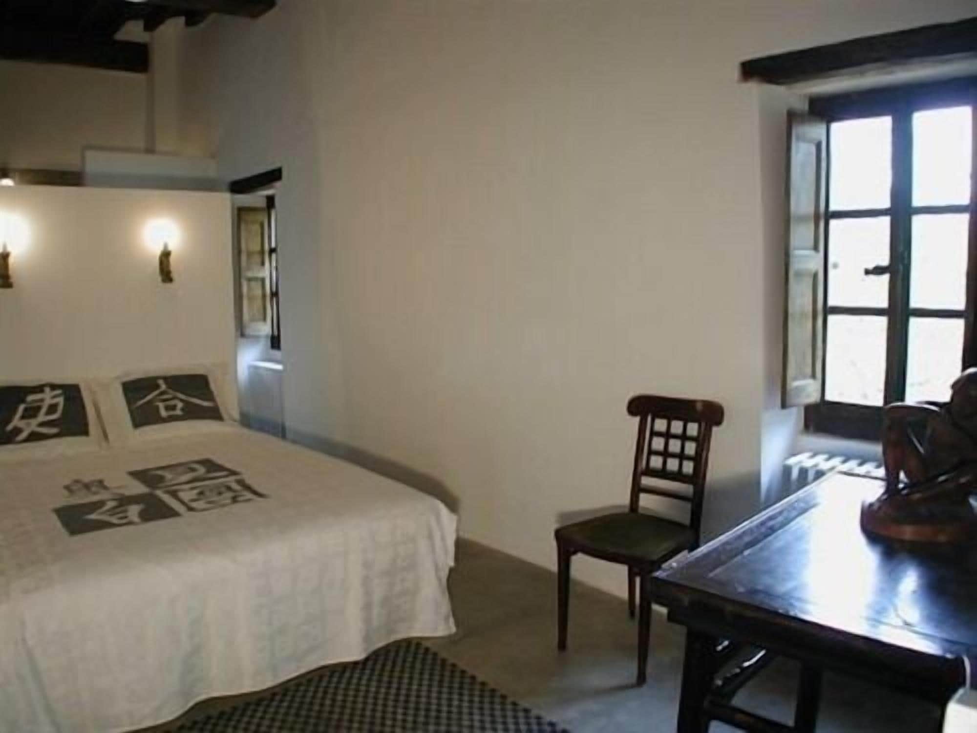 A bedroom with a bed, a chair, a table, and a window.