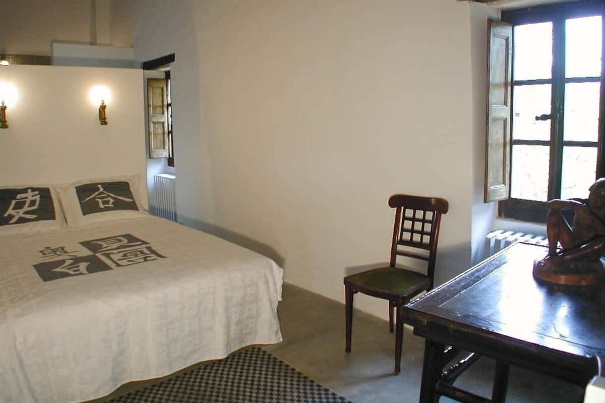A room with a bed, a chair, a table, and a window.