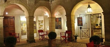 A courtyard with stone arches, red chairs, and potted plants.