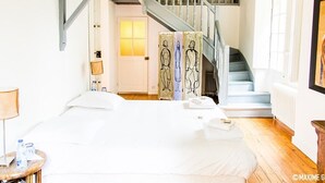 A hotel room with a bed, a nightstand, a lamp, a water bottle, a towel, a staircase, and a painting on the wall. - Château Beaupré Deleuze (Saint-Laurent-des-Arbres)