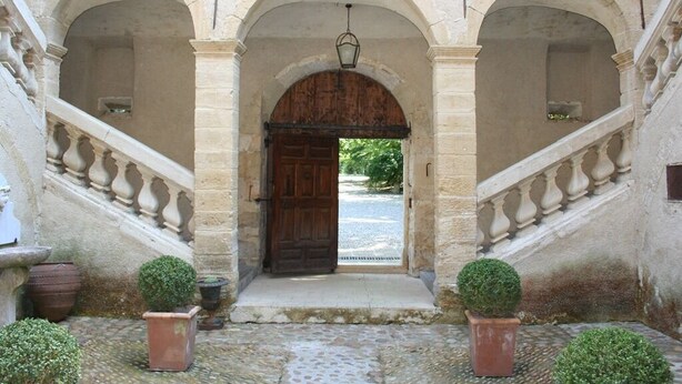 A stone entrance with a wooden door, flanked by two staircases and potted plants. - Château Beaupré Deleuze (Saint-Laurent-des-Arbres)