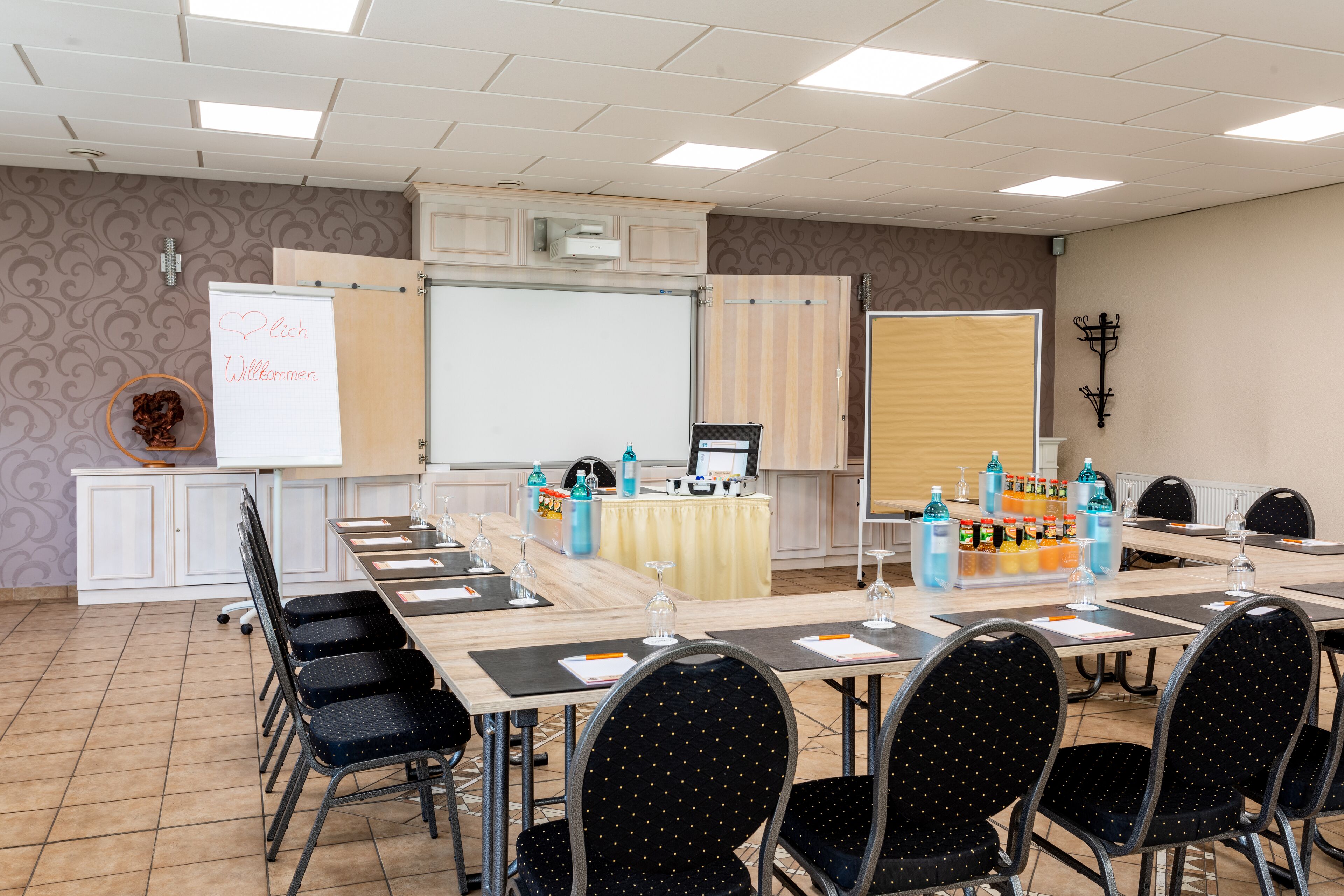 Ein Konferenzraum mit einem langen Tisch, schwarzen Stühlen, einer Whiteboard und einer Projektionsleinwand.