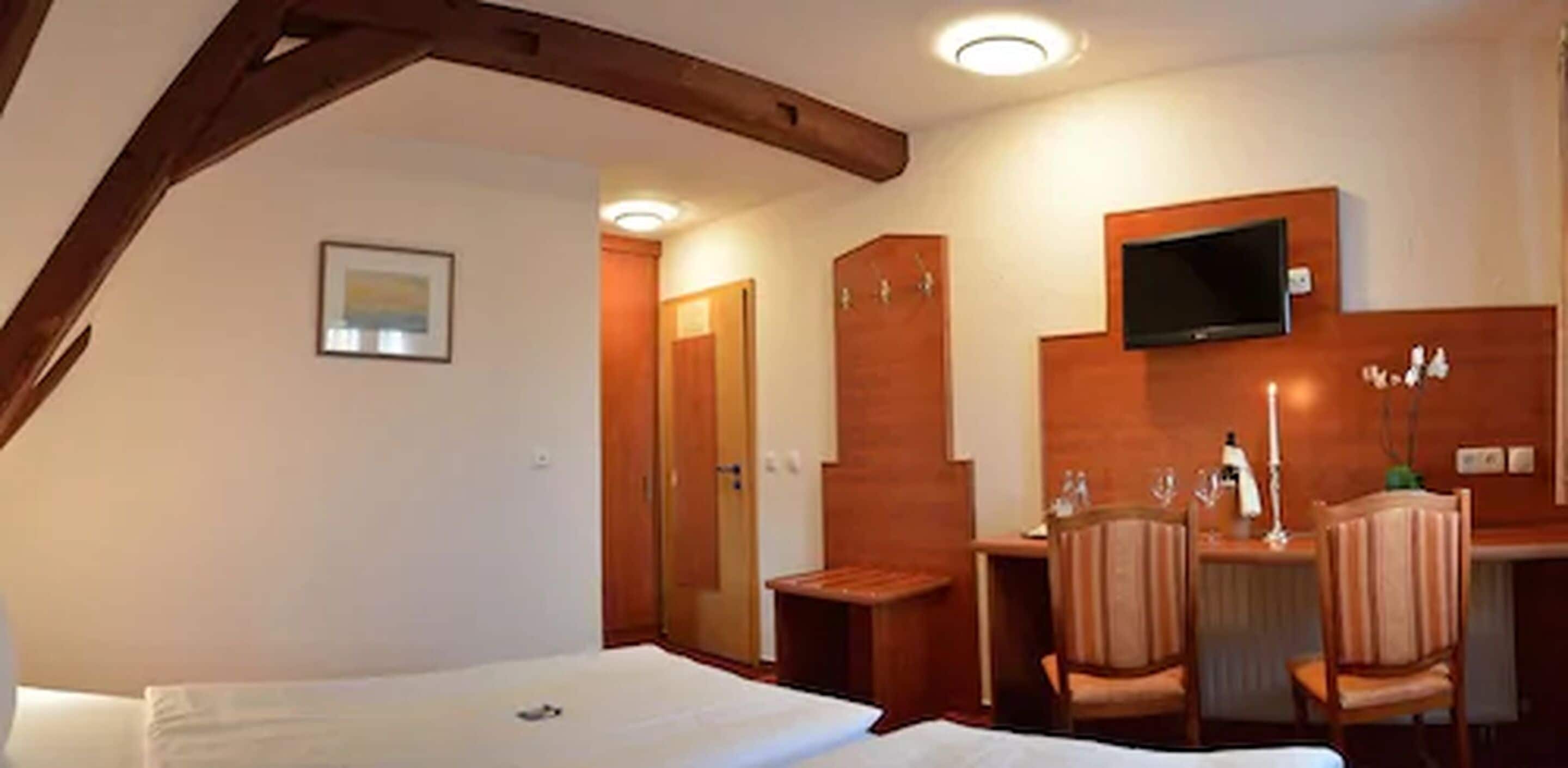 Una habitación de hotel con cama, escritorio con sillas, televisor y armario de madera.