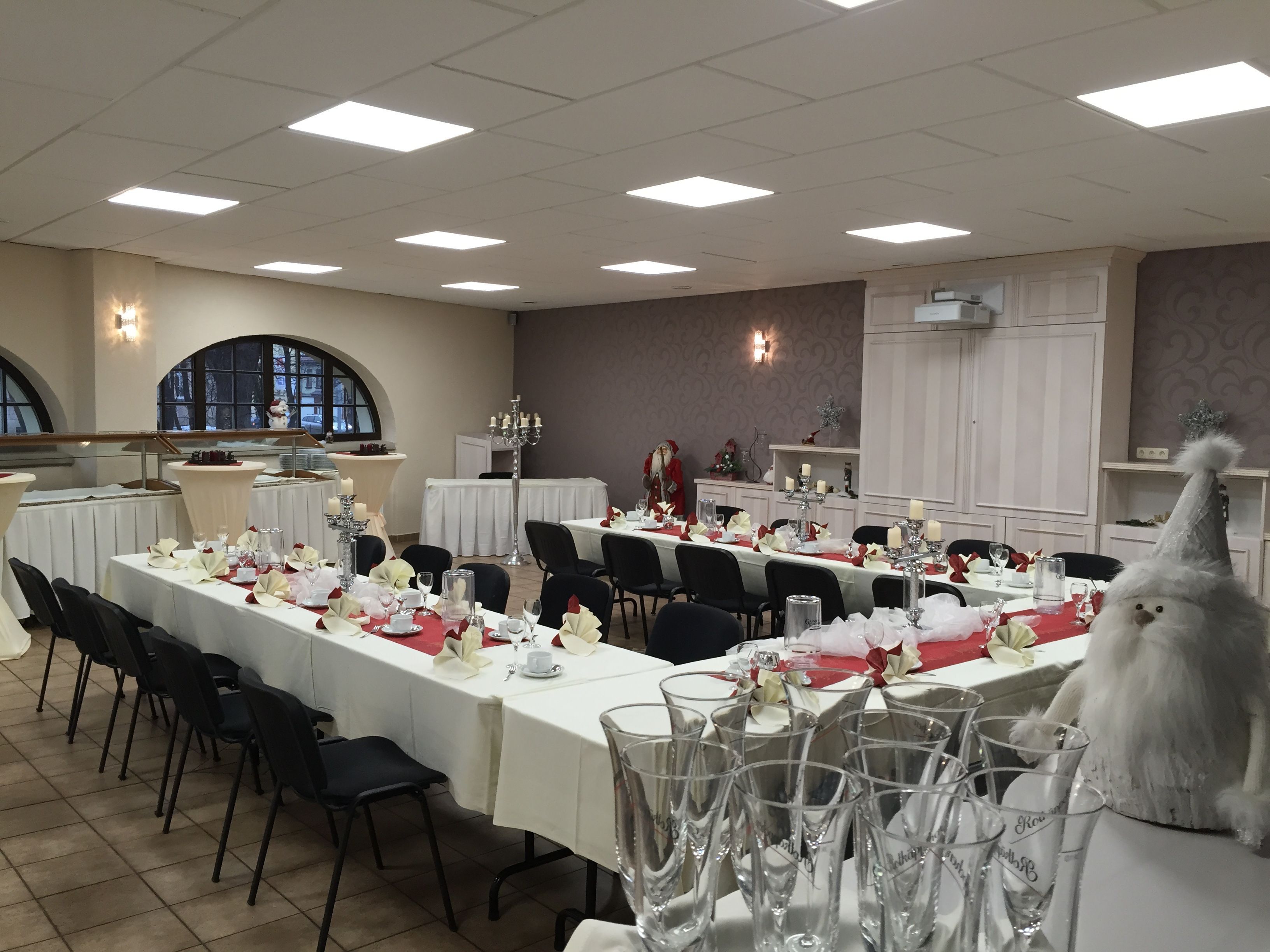 Ein Festsaal mit langen Tischen, gedeckt für eine festliche Veranstaltung, mit weißen Tischdecken, roten Servietten und Gläsern.