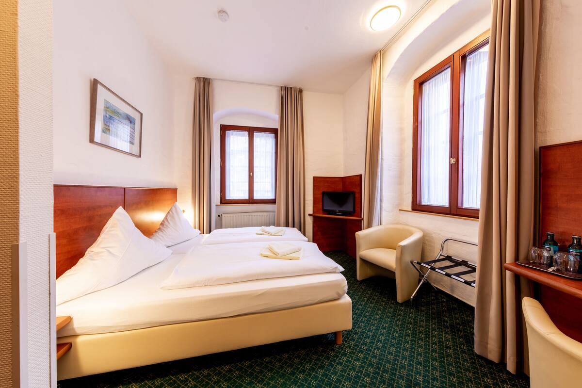 Hotellihuone, jossa on suuri sänky, työpöytä, jossa on televisio, tuoli ja ikkuna, jossa on verhot.