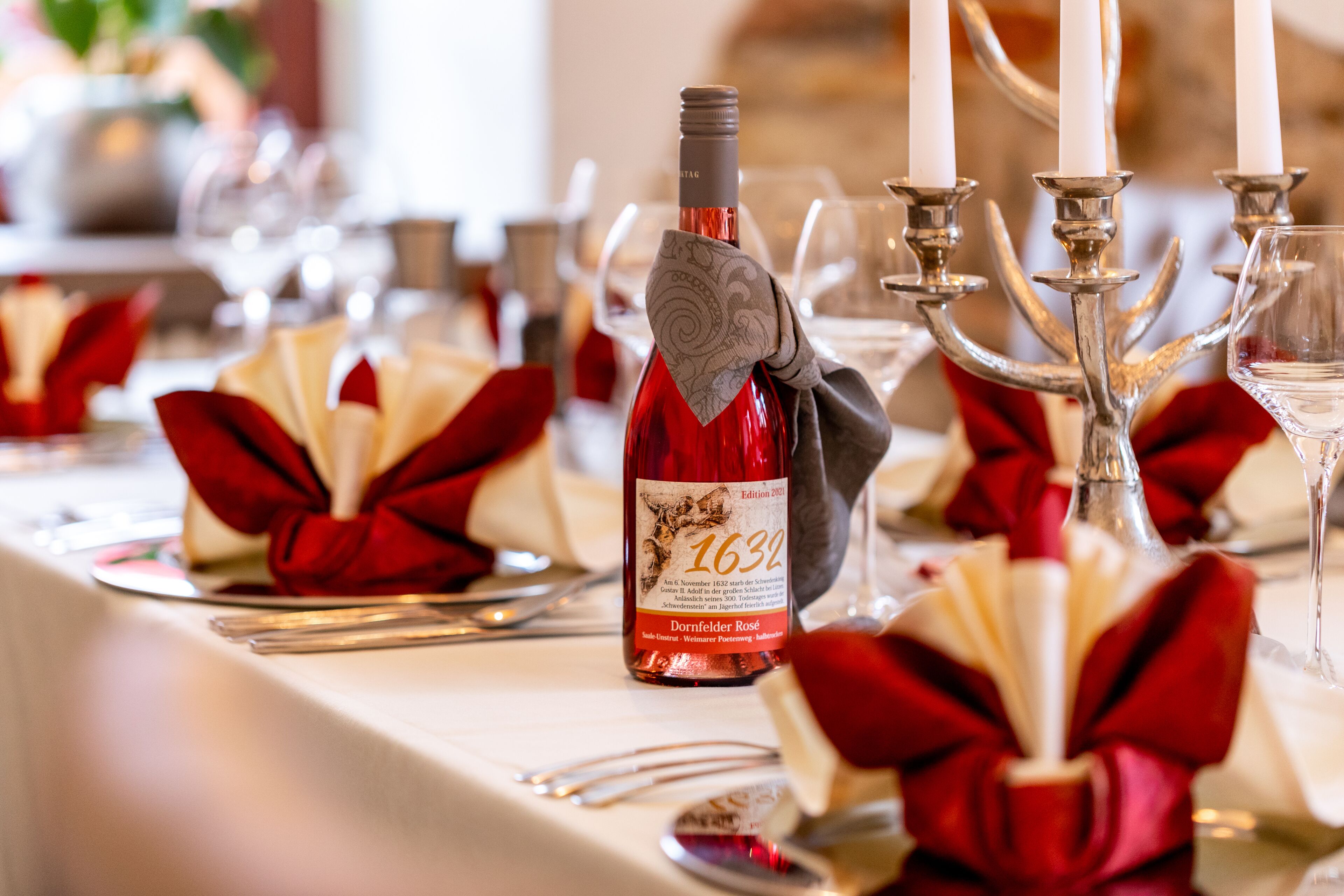 Una mesa dispuesta con servilletas rojas, una botella de vino y candelabros.