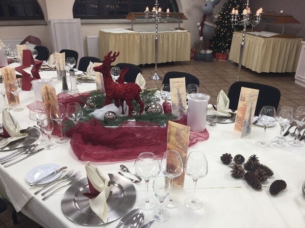 Una mesa decorada festivamente con un centro de mesa de ciervo rojo, velas y un árbol de Navidad al fondo.