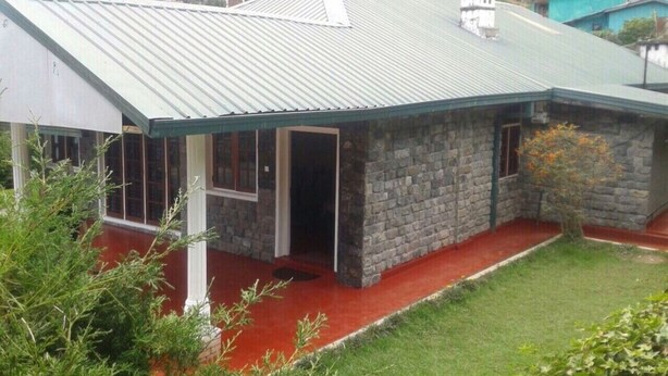 A stone building with a metal roof, a red porch, and a small garden area.