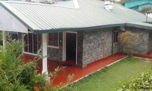 Un edificio de piedra con techo metálico, un porche rojo y un pequeño jardín.