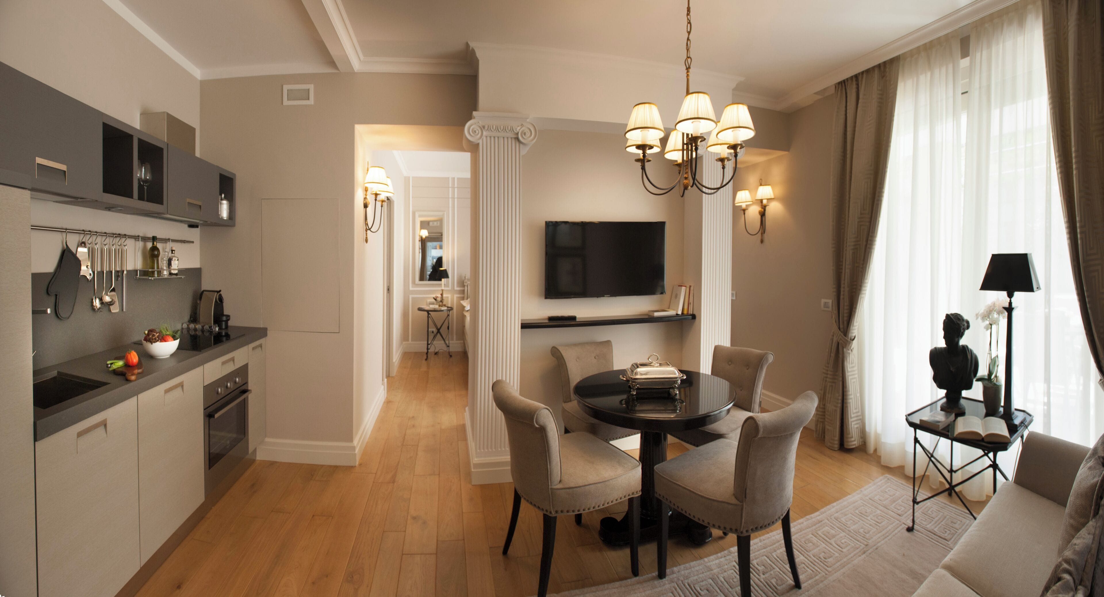 A modern hotel room with a dining area, kitchen, and a living space with a TV and decorative items.