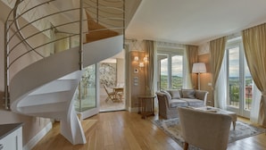 Un interior moderno con una escalera de caracol, una sala de estar con sofá y sillones, y un comedor con mesa y sillas.