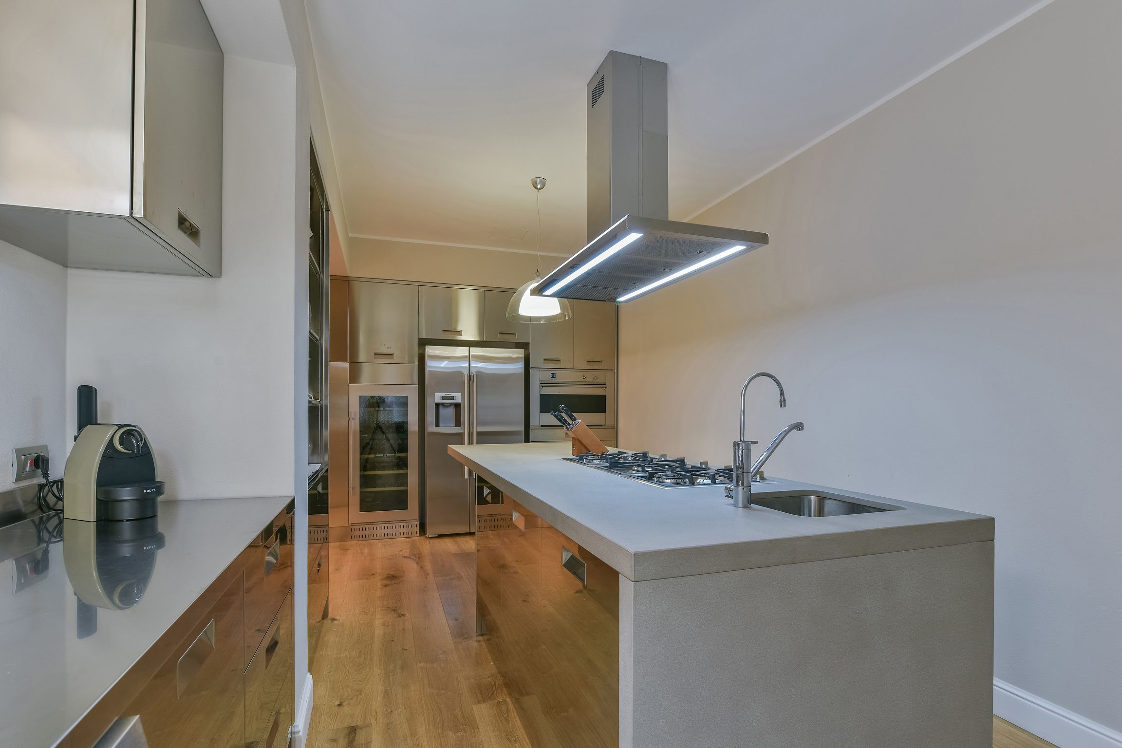 A modern kitchen with a central island, stainless steel appliances, and a built-in oven.