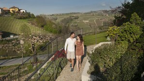 Una pareja camina por una escalera de piedra con barandilla de metal, rodeada de vegetación y con vistas a un paisaje montañoso.