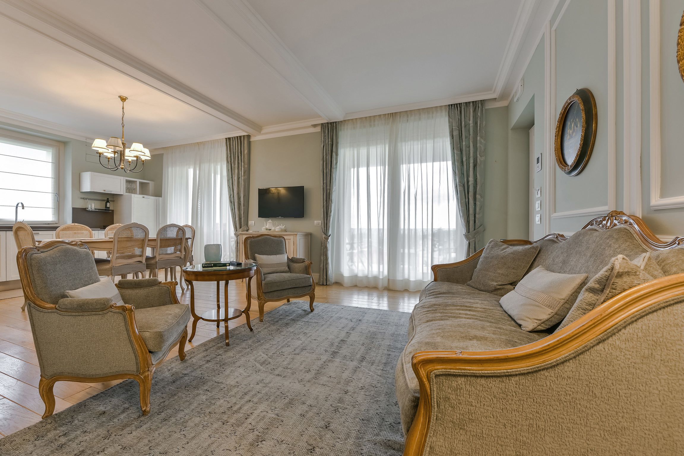 A spacious living room with a large sofa, armchairs, a dining table, and a television.