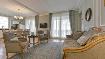 A spacious living room with a large sofa, armchairs, a dining table, and a television.