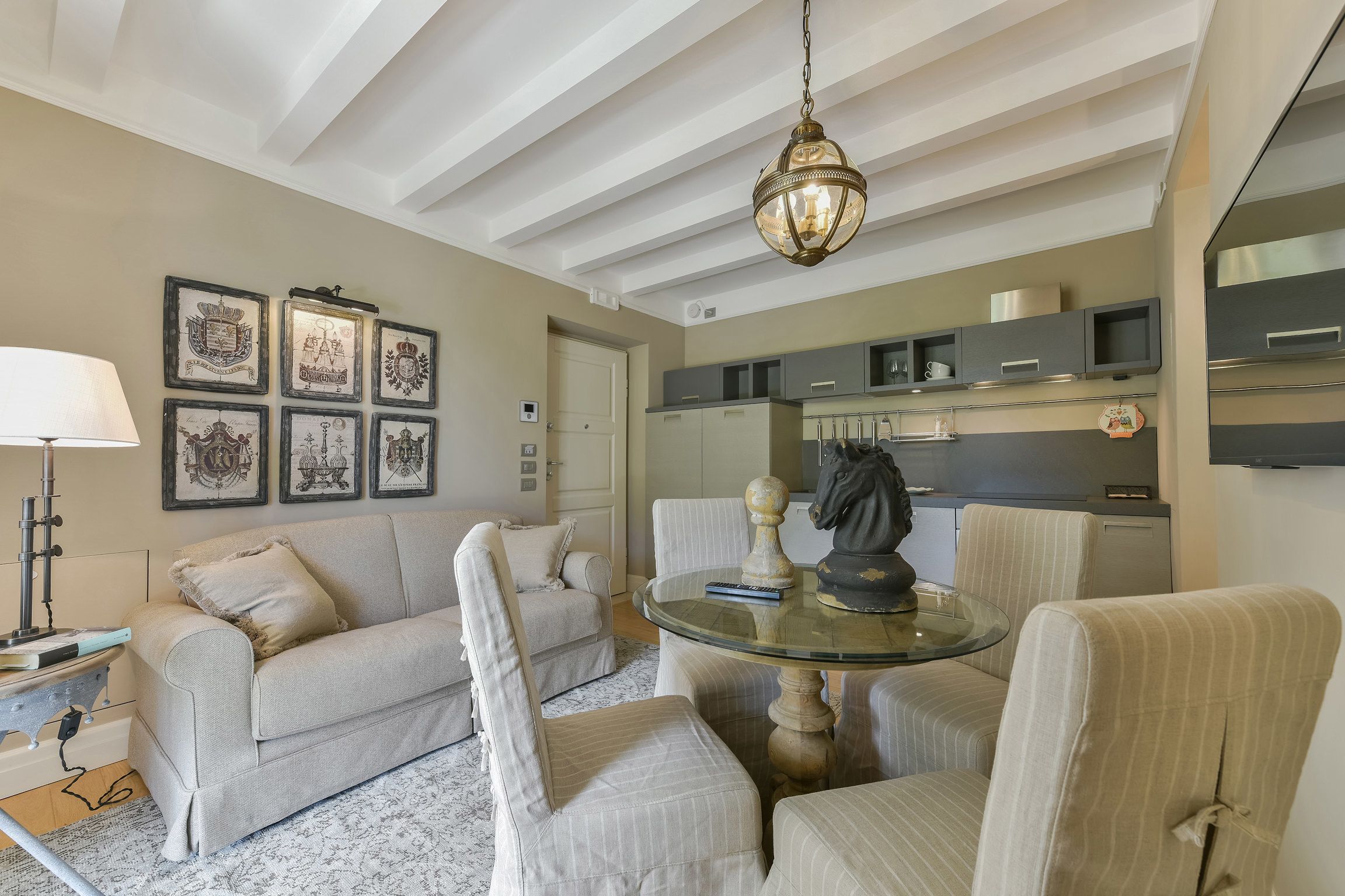 A living room with a sofa, armchairs, a glass coffee table, and a ceiling light fixture.