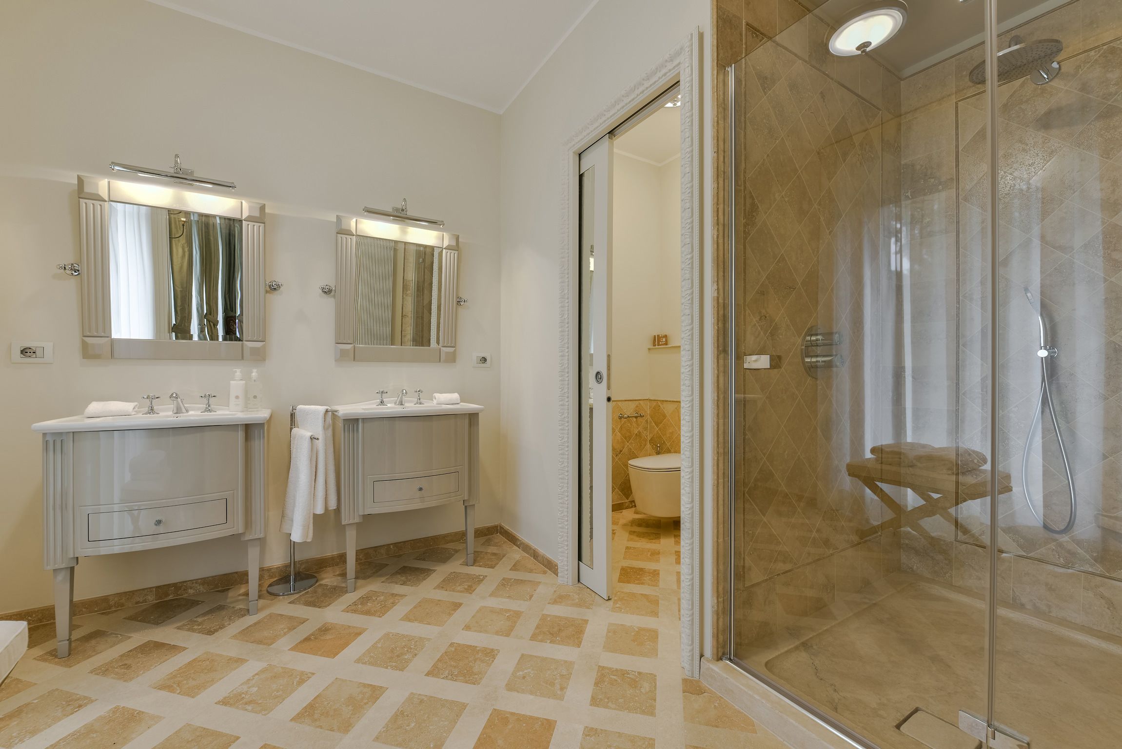 A modern bathroom with two sinks, a glass shower enclosure, and a toilet visible through an open door.