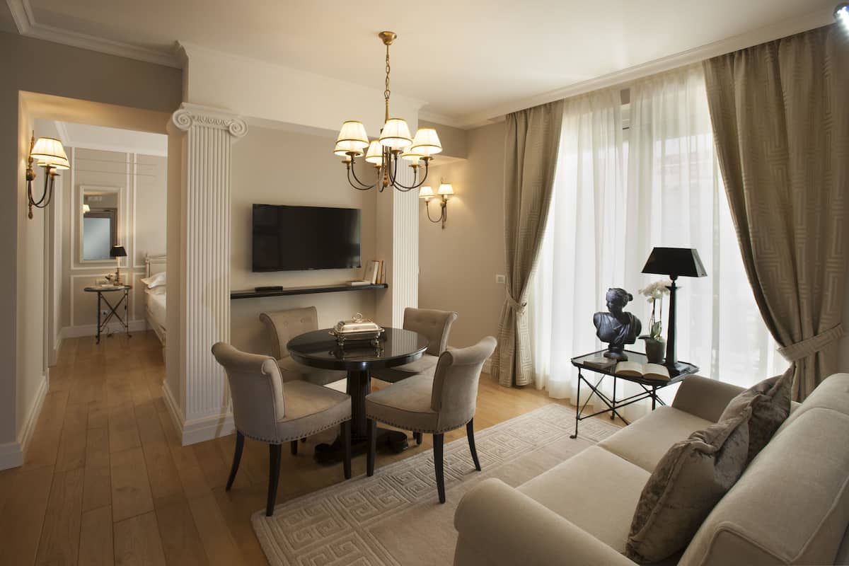 A modern living room with a dining area, a flat-screen TV mounted on the wall, and a sofa with a decorative pillow.