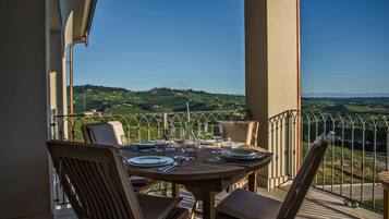 A round wooden table set for dining with chairs, a view of green hills and a clear sky.