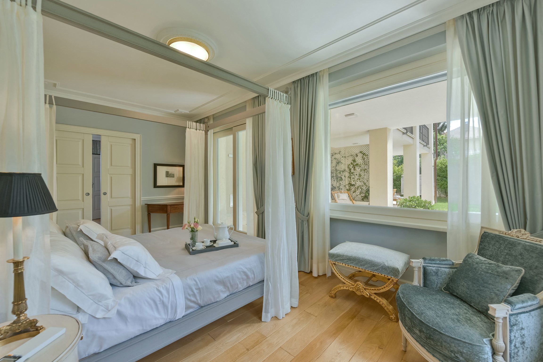 Un dormitorio con cama, mesita de noche, lámpara y vistas al exterior.