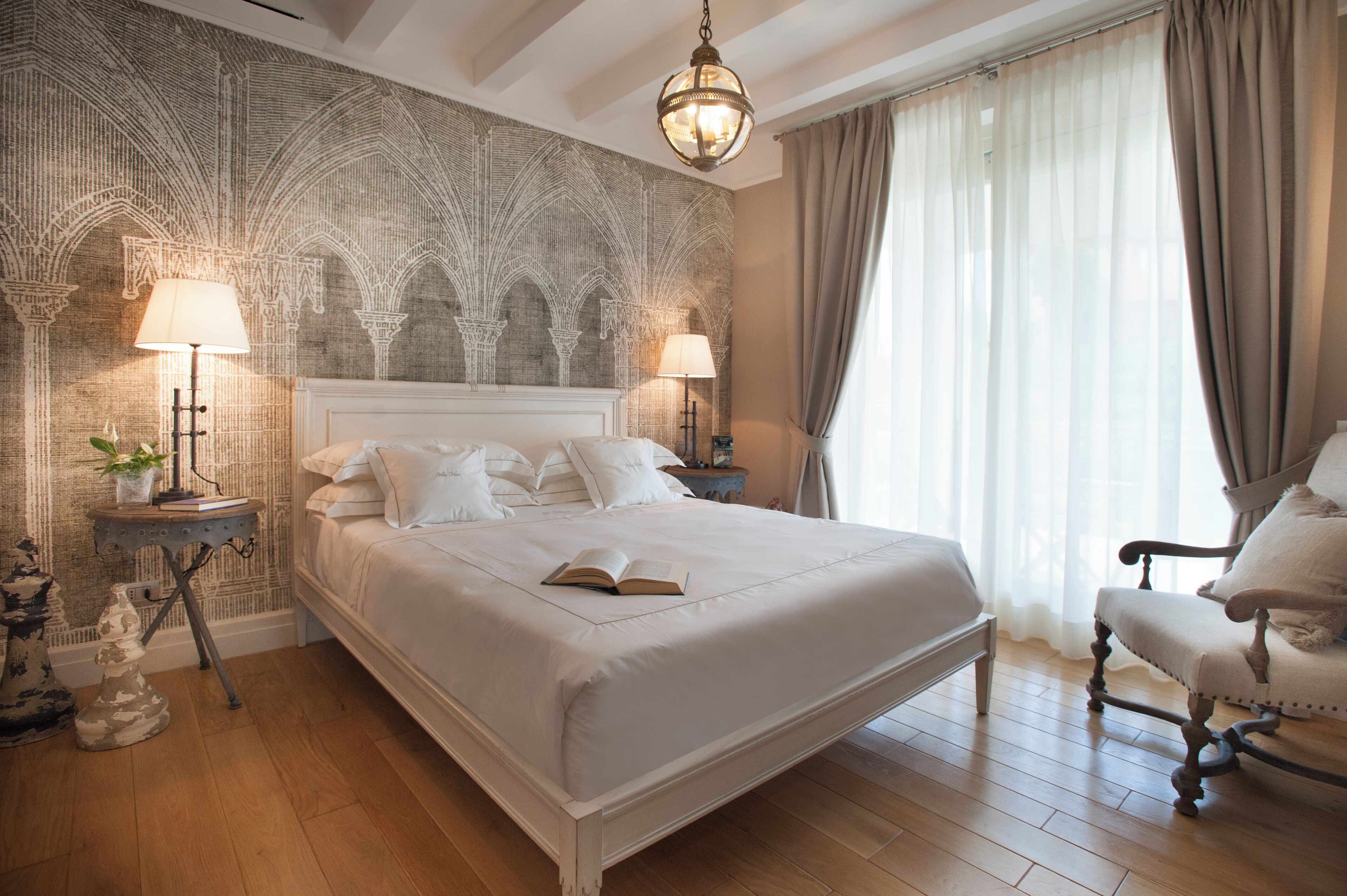 A spacious bedroom with a large bed, two bedside tables with lamps, a decorative wall, and a chair.