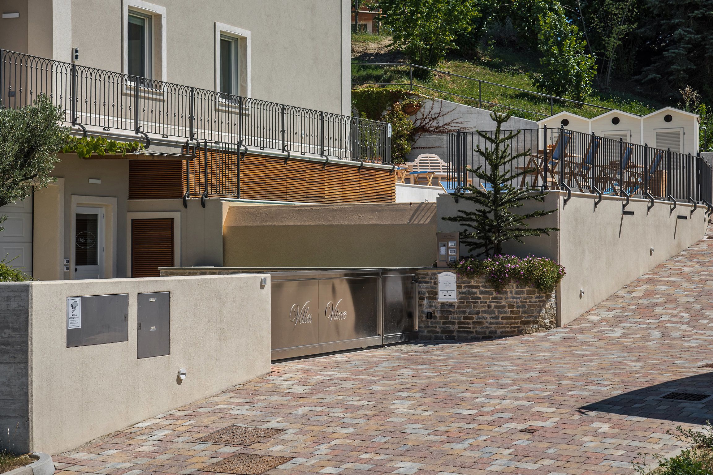 Un edificio residencial con entrada protegida, cerca de madera con listones y un camino pavimentado que conduce a una zona cerrada.