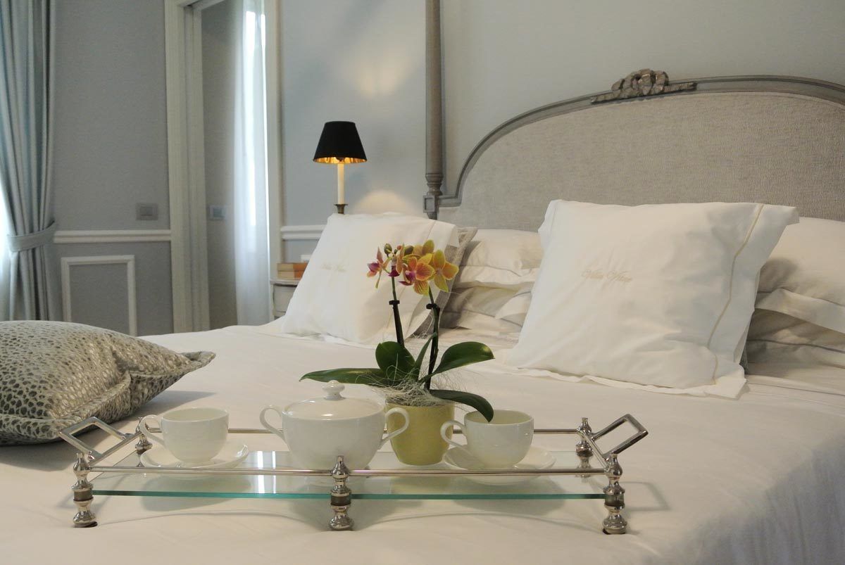 A neatly made bed with white linens, a glass tray with tea set, and a potted orchid.