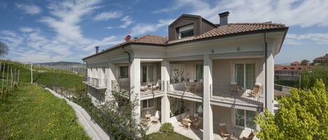 A modern two-story house with a balcony, a patio with outdoor furniture, and a view of the surrounding landscape.