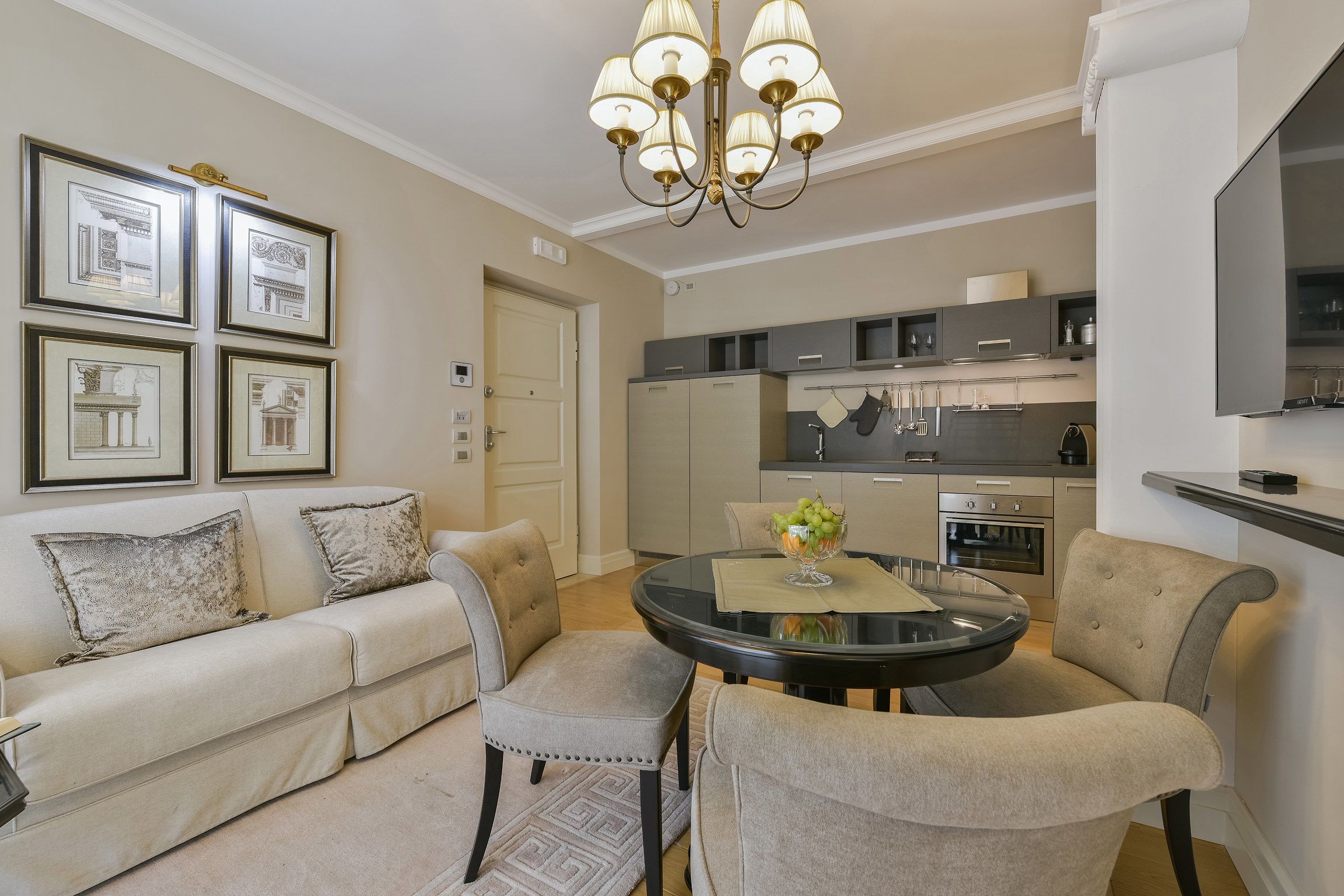 A modern living room with a sofa, chairs, a round table, and a chandelier.