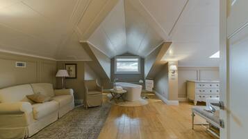 Ruime slaapkamer op zolder met een groot raam, een wit bad, een bank, een stoel en een dressoir.