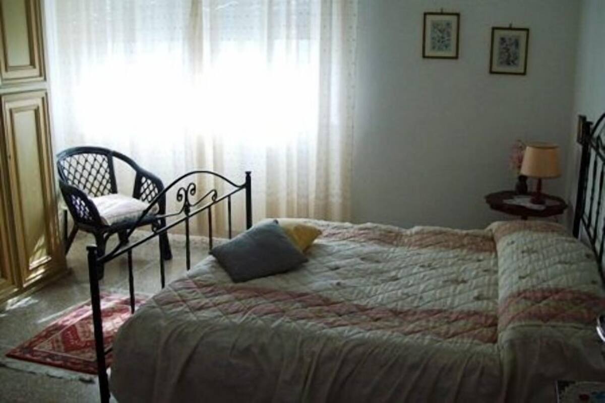 A bedroom with a bed, a chair, a nightstand, and a window with curtains.
